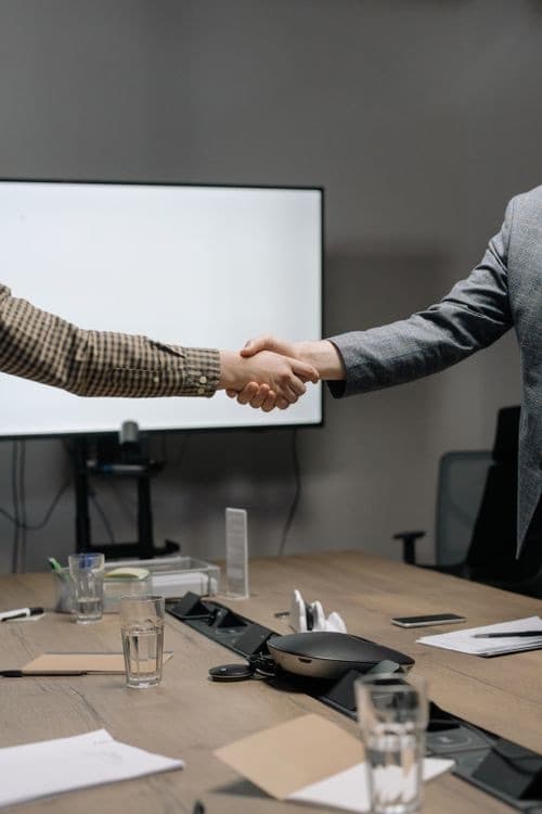 Two people shaking hands across a boardroom table