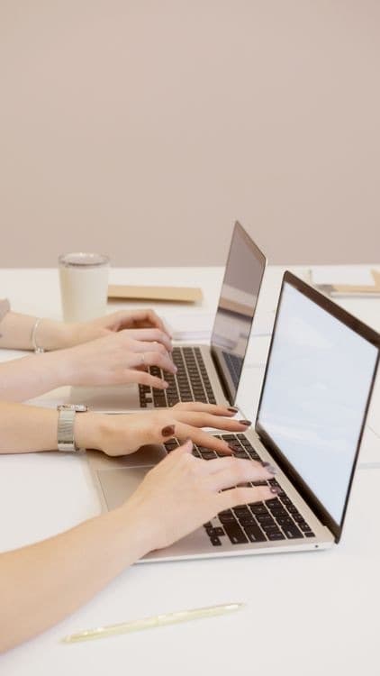 Two people working side by side on laptops at a white desk